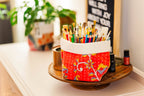 Colorful paintbrush holder on a table with plants and a chalkboard in the background