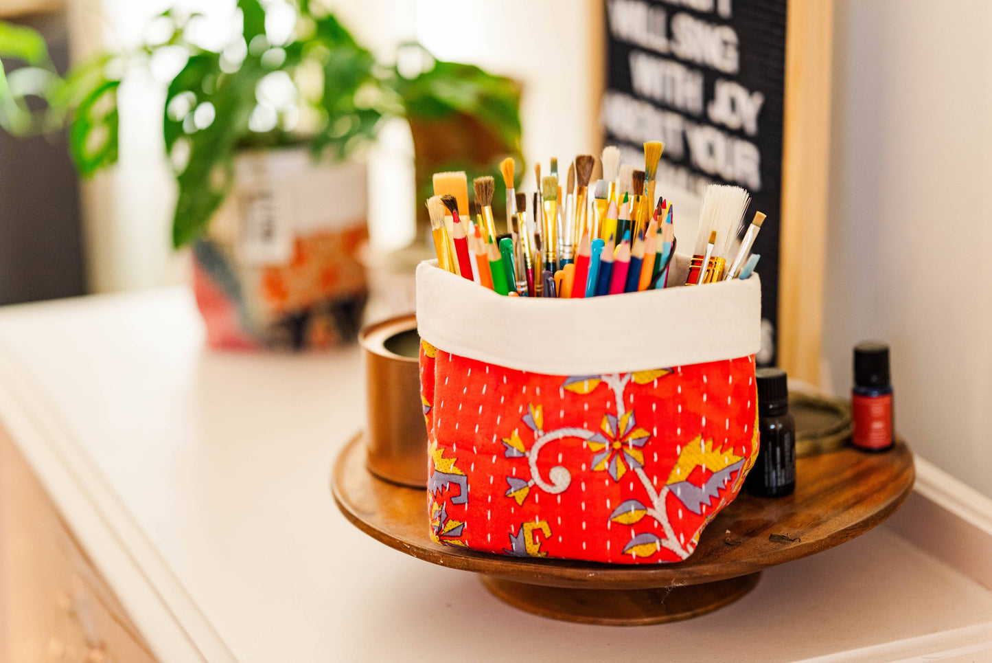 Colorful paintbrush holder on a table with plants and a chalkboard in the background