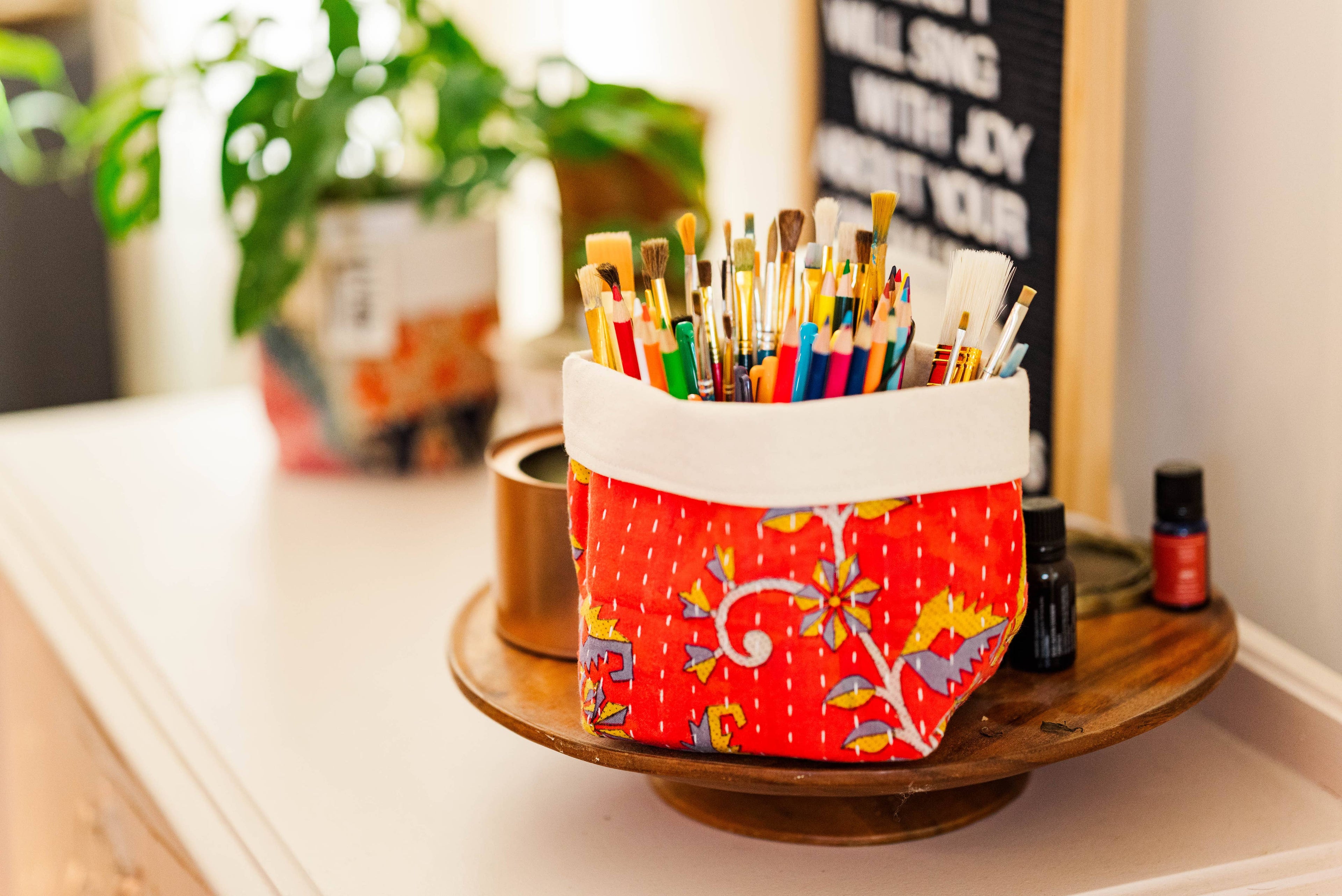 Colorful paintbrush holder on a table with plants and a chalkboard in the background