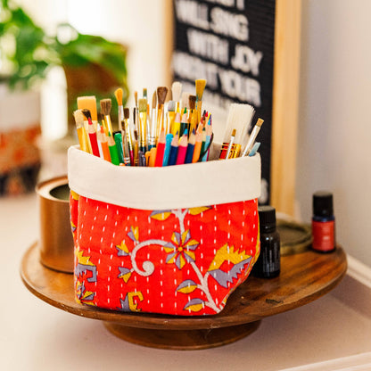 Colorful paintbrush holder on a table with plants and a chalkboard in the background