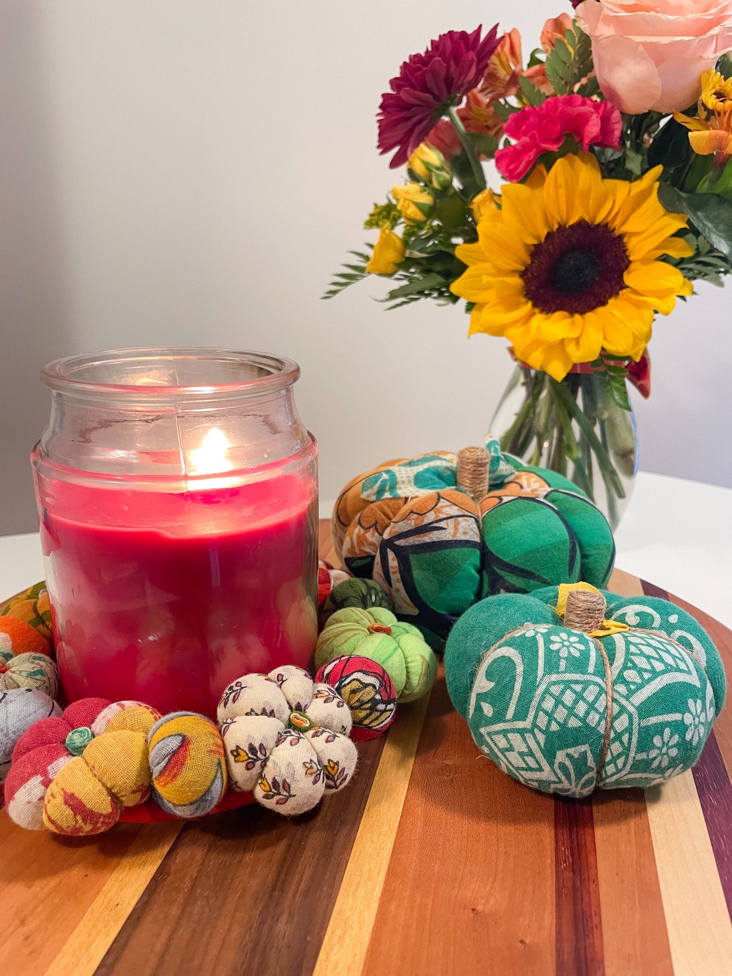 Decorative pumpkins with colorful patterns next to a lit pink candle on a wooden surface.