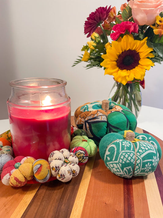 Decorative pumpkins with colorful patterns next to a lit pink candle on a wooden surface.