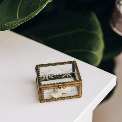 A Beautiful glass box with etched stars displayed on a white tabletop with plants in the background 