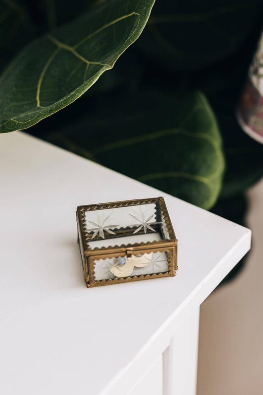 A Beautiful glass box with etched stars displayed on a white tabletop with plants in the background 