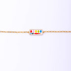 Delicate Paint Box Bracelet with a gold gilt enamel charm, presented in a matchbook-style box with a punch-hole for hanging.
