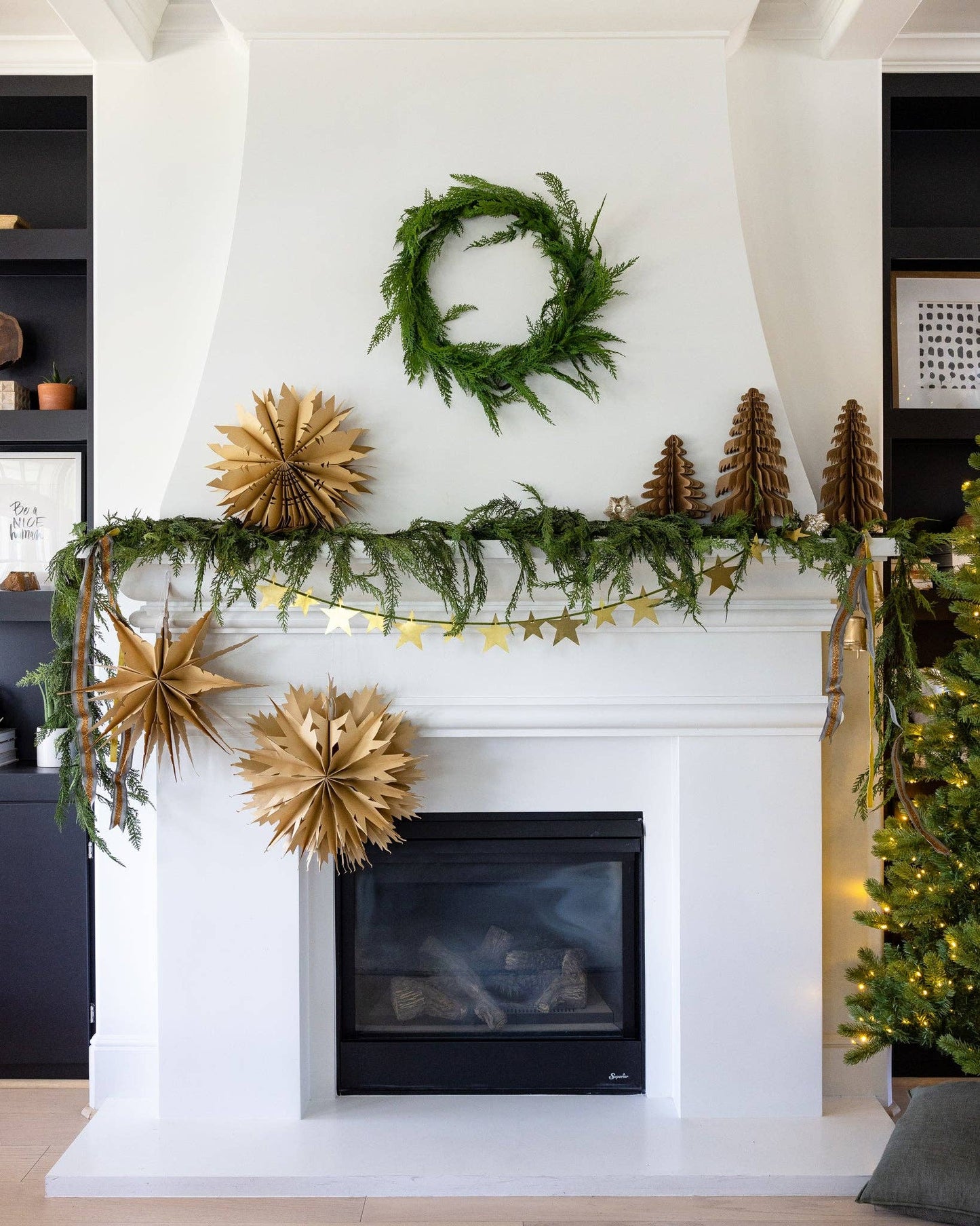 Decorative fireplace mantel with greenery, gold stars, and a wreath above a white fireplace.