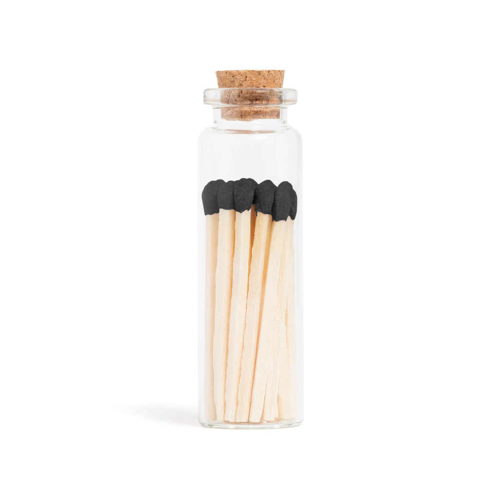 Black matchsticks in a corked glass vial with a match striker at the bottom.