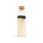 Black matchsticks in a corked glass vial with a match striker at the bottom.