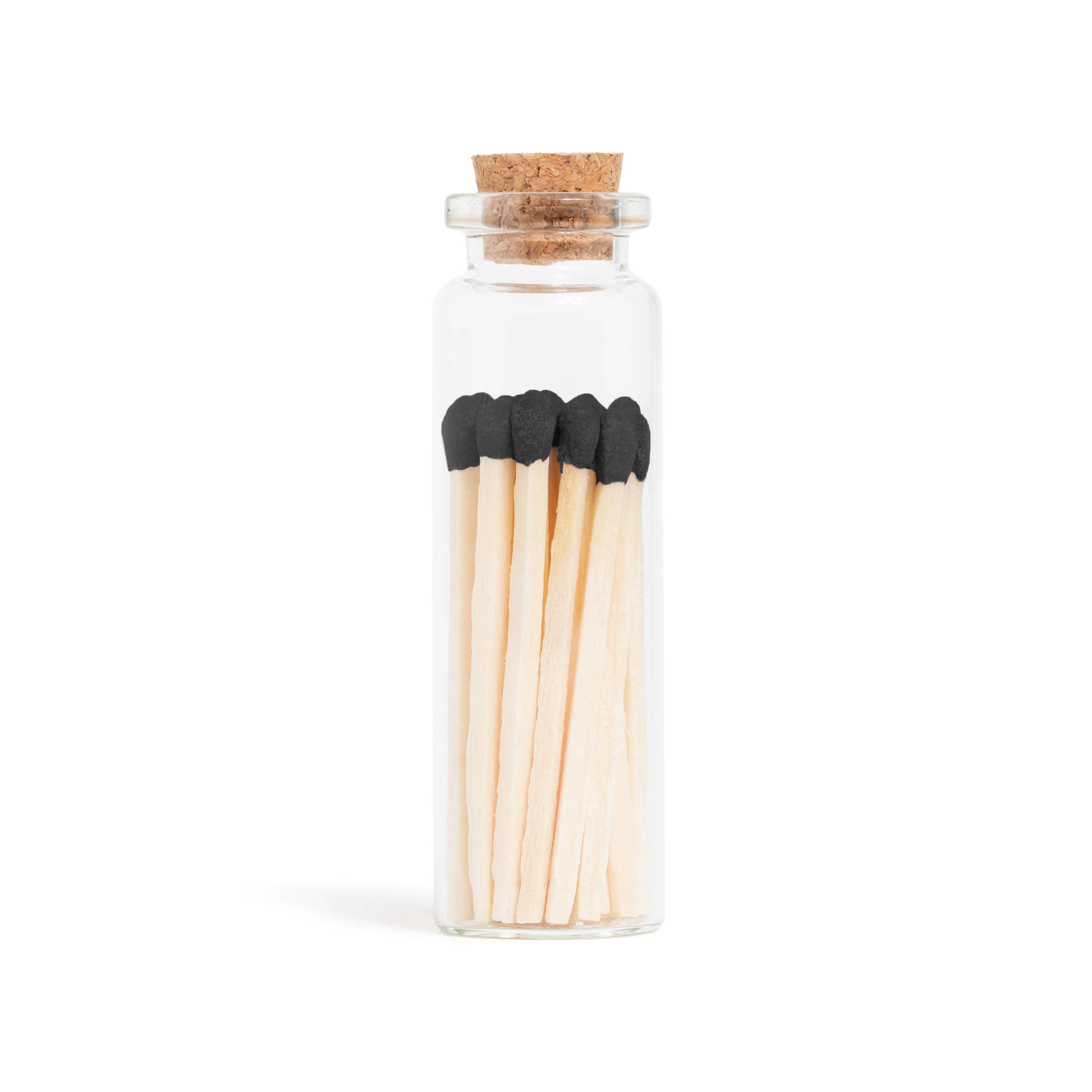 Black matchsticks in a corked glass vial with a match striker at the bottom.