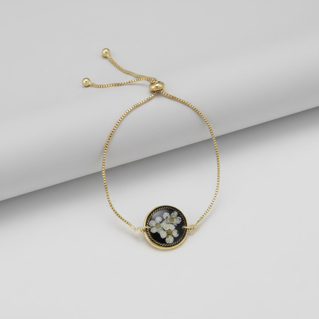 Gold bracelet with a black and white floral pendant on a white background
