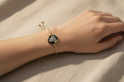 Gold bracelet with a black and white floral pendant worn on a wrist with a neutral background