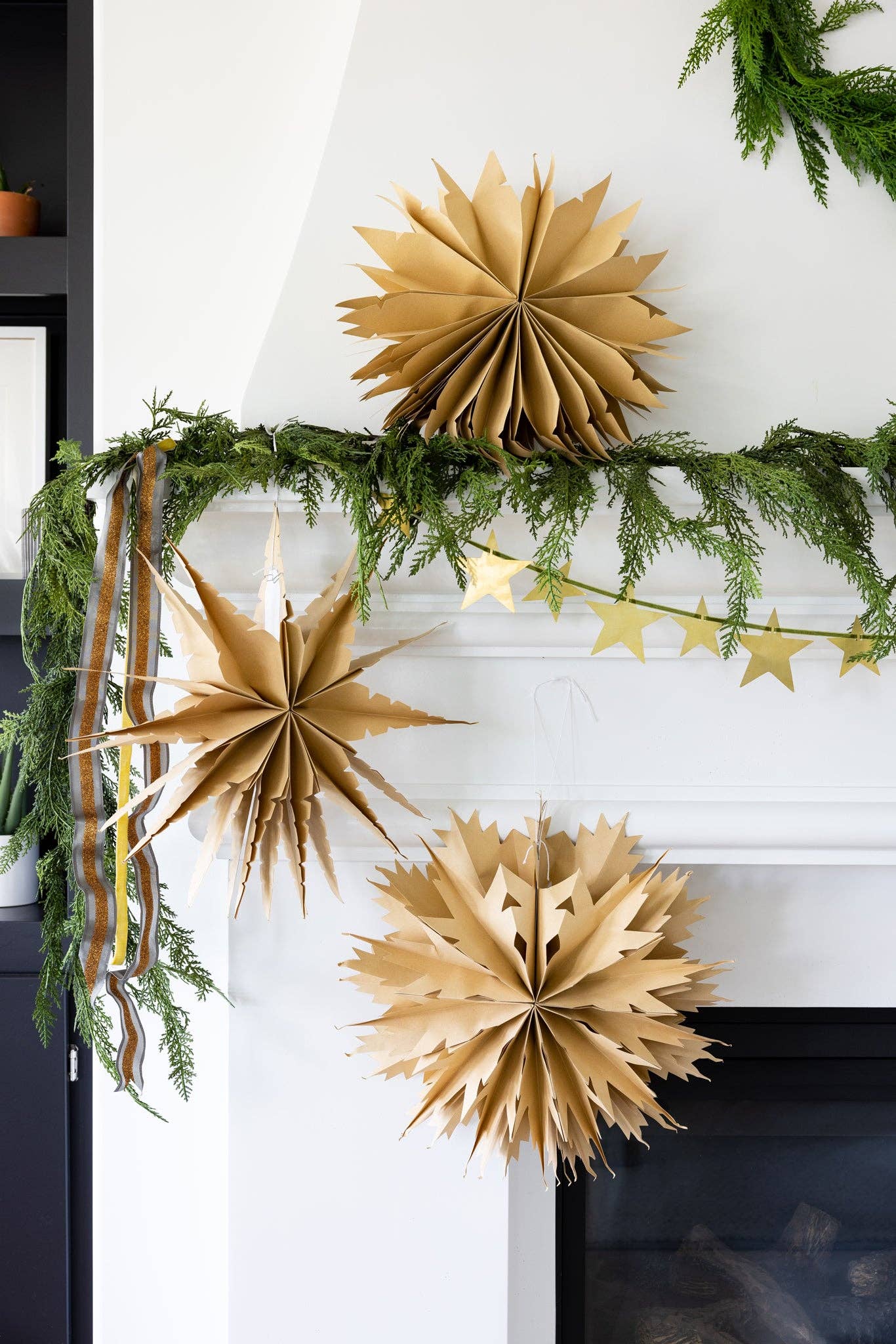 Decorative gold paper stars and greenery on a mantelpiece.