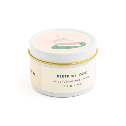 Birthday cake scented candle in white tin with corked vial of colorful matchsticks, packaged in a clear vinyl gift box.