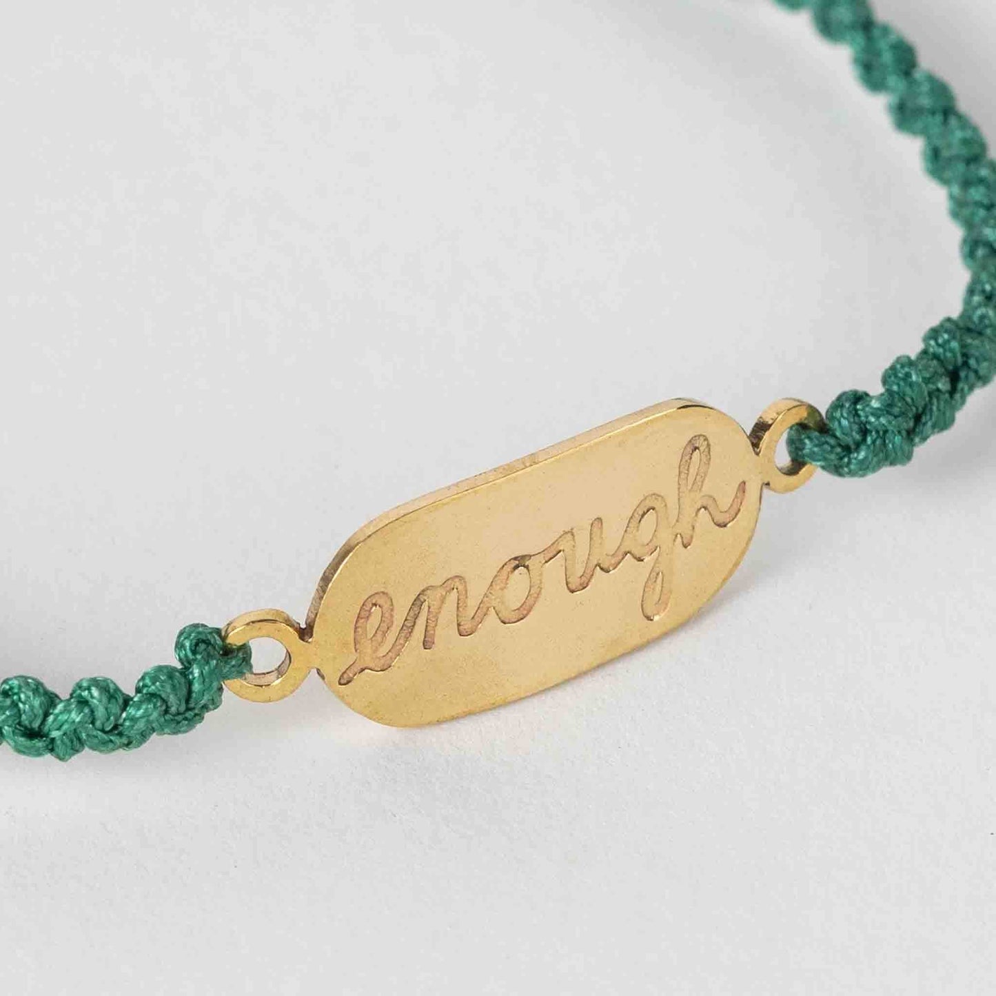 Close-up of artisan-made bracelet featuring bold brass affirmation on green nylon cord
