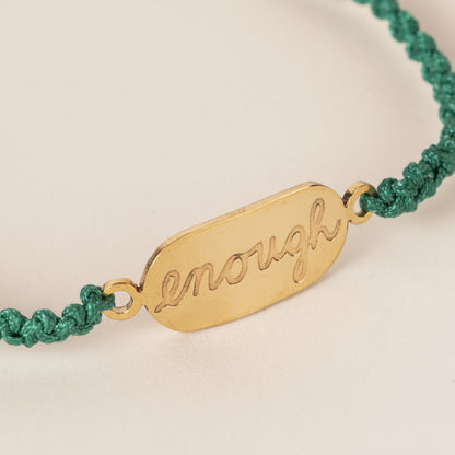 Close-up of artisan-made bracelet featuring bold brass affirmation on green nylon cord