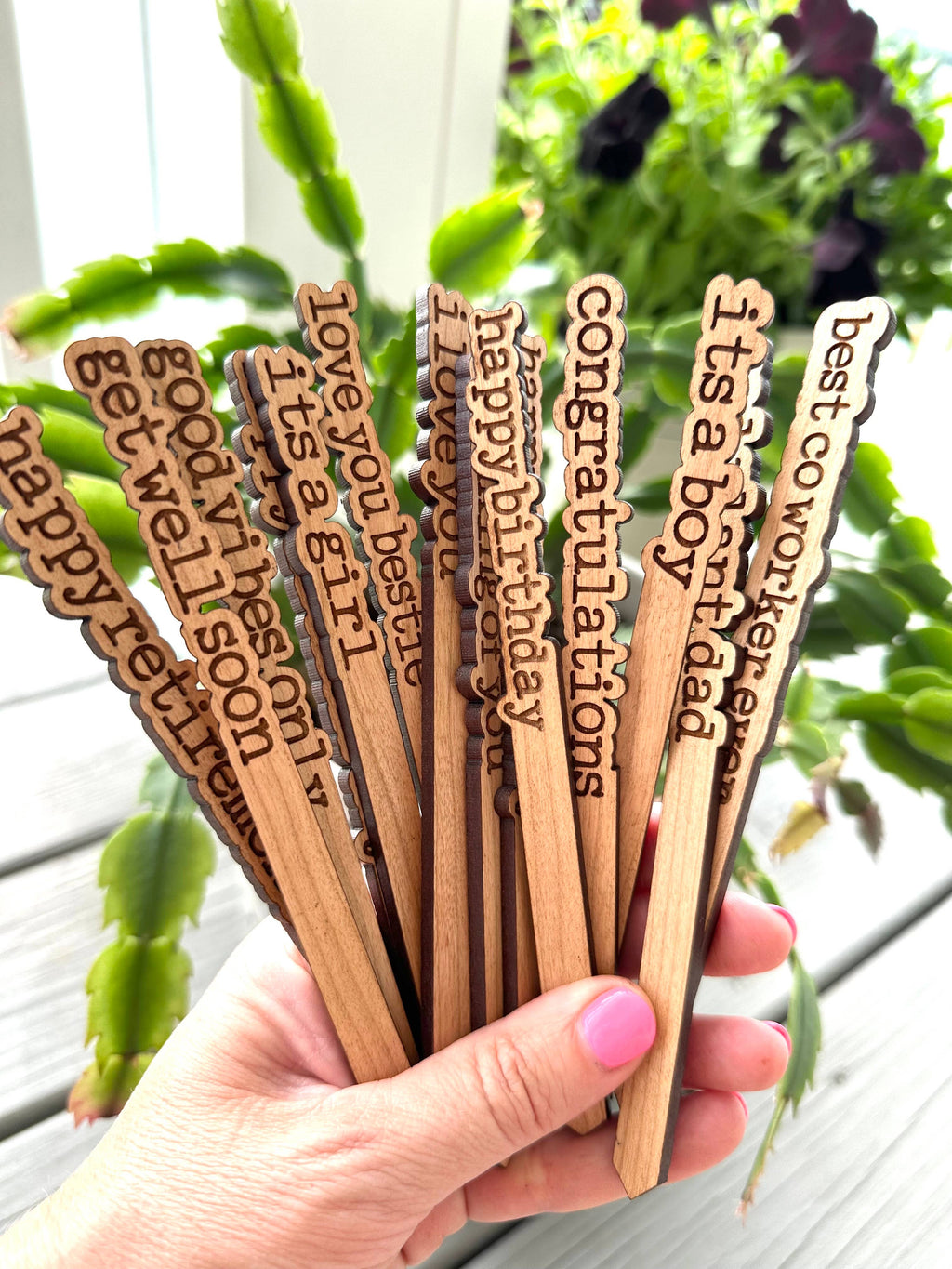 Close-up of wooden plant markers reading "I Love You," "Thinking of You," and "Good Vibes Only."