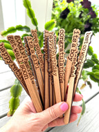 Close-up of wooden plant markers reading "I Love You," "Thinking of You," and "Good Vibes Only."