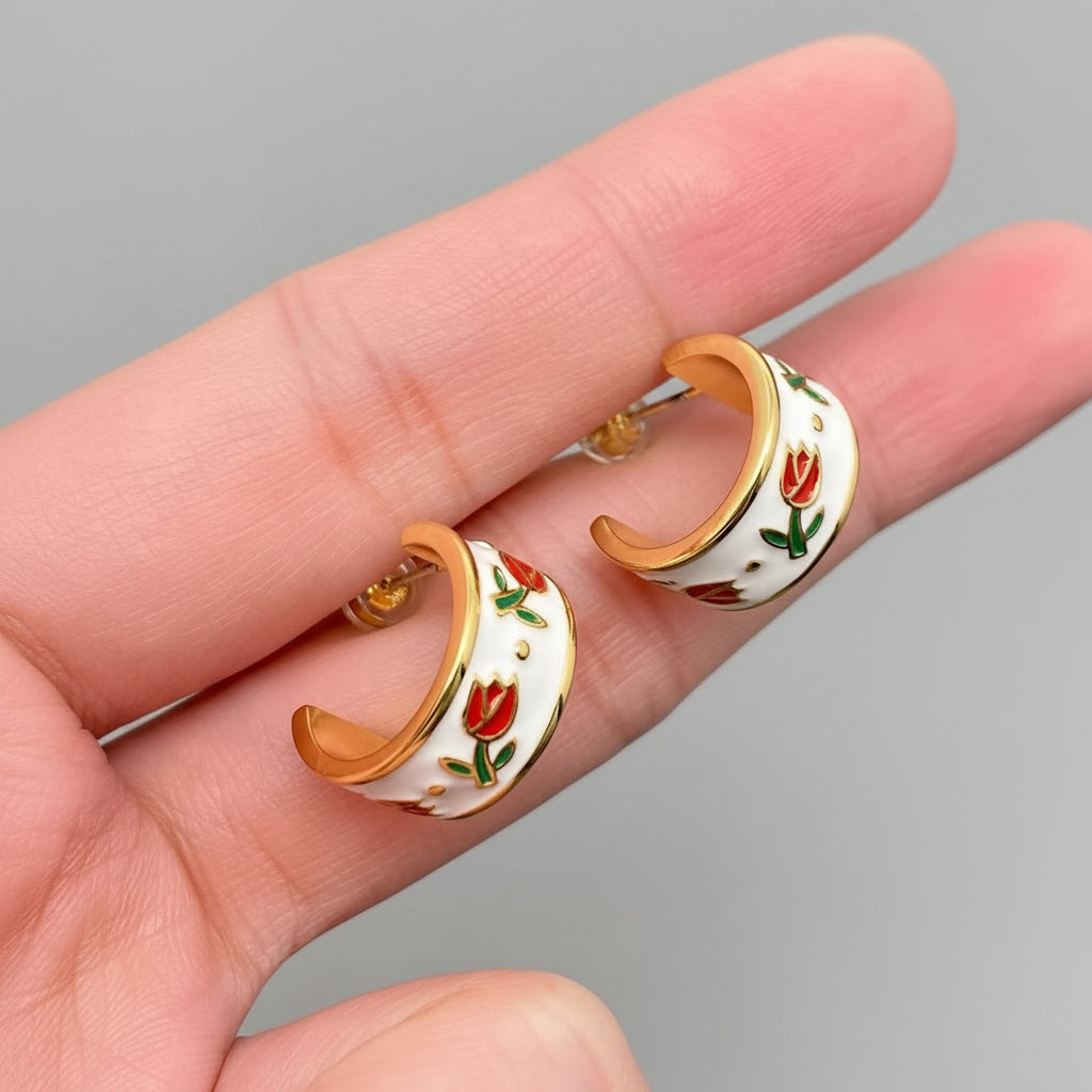 Gold and white floral earrings held between fingers on a gray surface