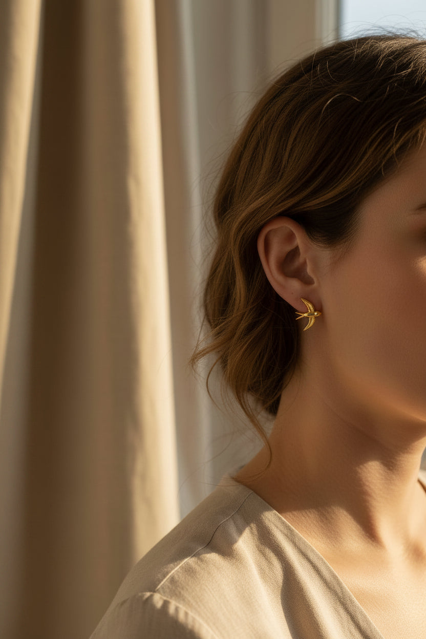 Gold bird-shaped earrings on a white card with a blurred indoor background