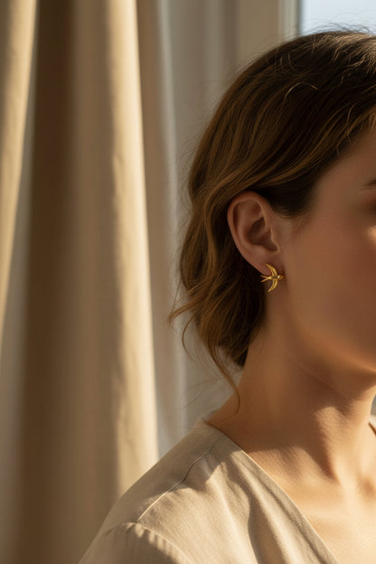 Gold bird-shaped earrings on a white card with a blurred indoor background