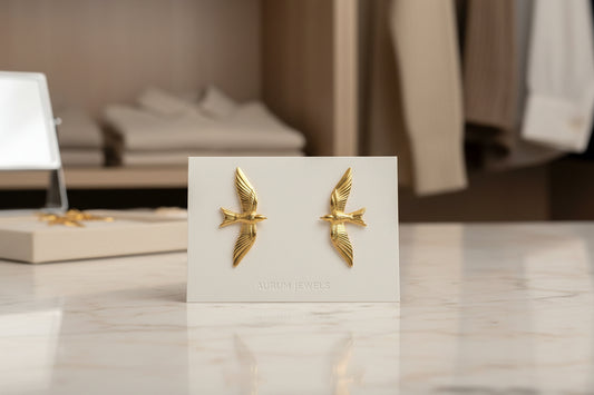 Gold bird-shaped earrings on a white card with a blurred indoor background
