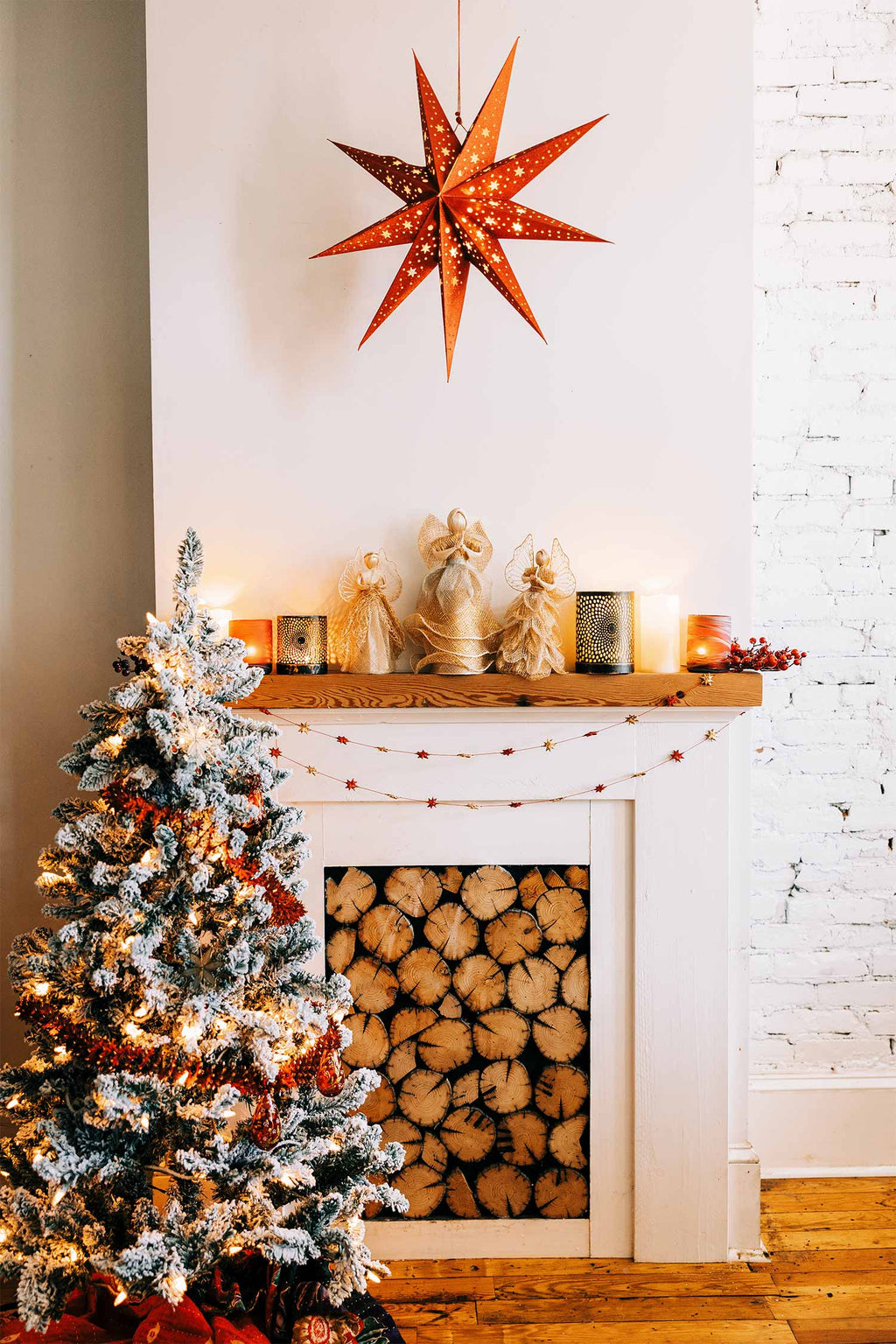 Decorated Christmas tree with a star-shaped light fixture above, next to a white brick wall. The Red & Gold Palm Star Garland hangs on the mantel.