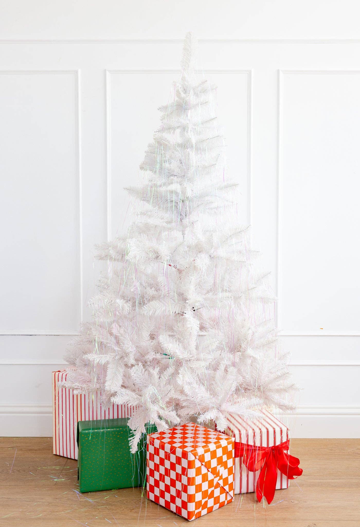 White Christmas tree with colorful presents against a white wall