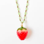 Necklace styled on neutral background with soft shadows emphasizing the glossy red strawberry charm