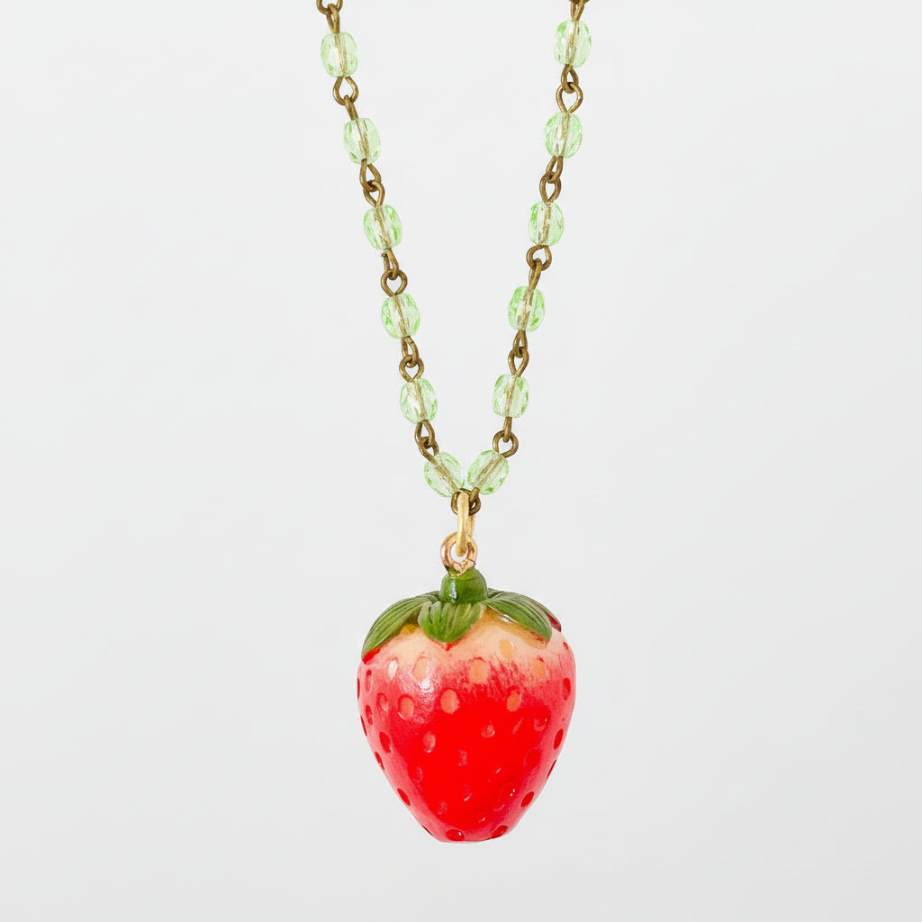 Necklace styled on neutral background with soft shadows emphasizing the glossy red strawberry charm