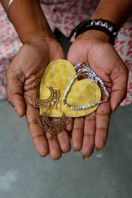 Hands holding two yellow heart-shaped heart gift pouch with decorative earrings on a blurred background