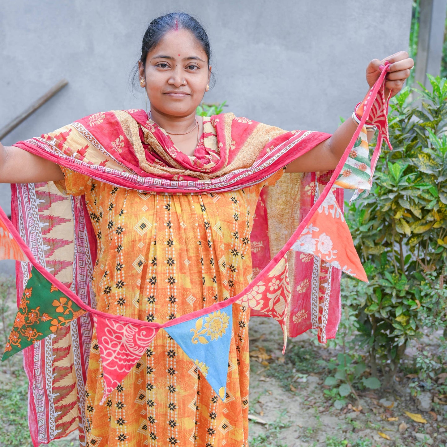 A woman from Asha Projects holding a colorful garland in front of a gray wall