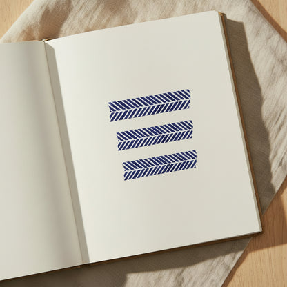 Three navy and white herringbone striped washi tape strips on a white journal page on a tabletop with a natural textile