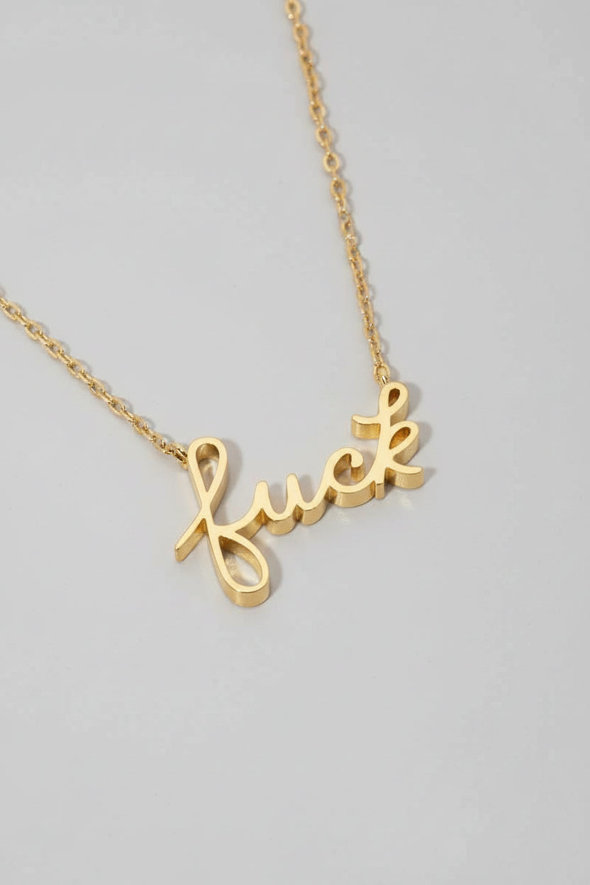 A gold-dipped pendant necklace with the word 'Fuck' written in cursive on a light-colored surface.