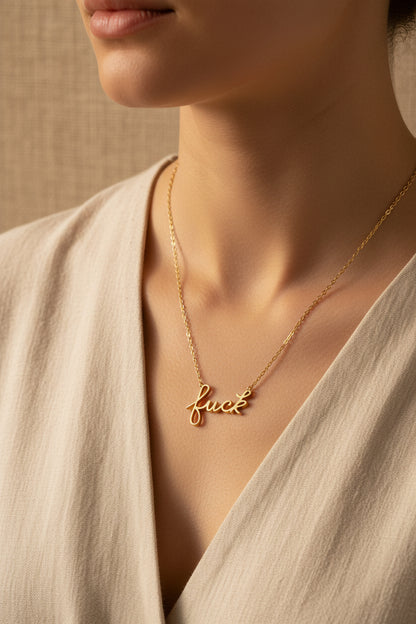 A gold-dipped pendant necklace from Rochambeau Home with the word 'Fuck' written in cursive worn with a neutral background