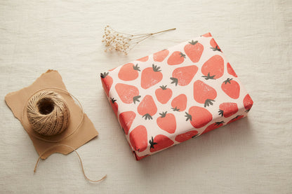 Strawberry embellished gift wrap showcased wrapped around a gift with twine and flowers on a beige background