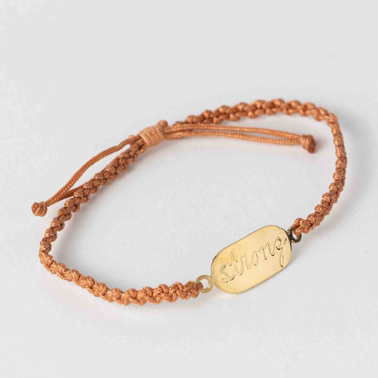 Bracelet with a gold tag and brown cord on a light gray background