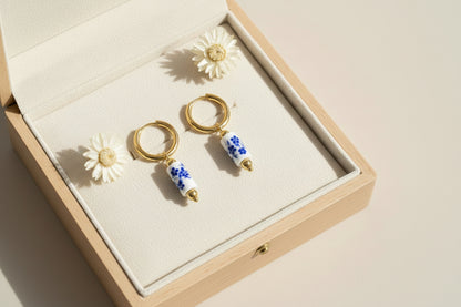 Pair of gold earrings with blue floral beads in a jewelry box on a light background