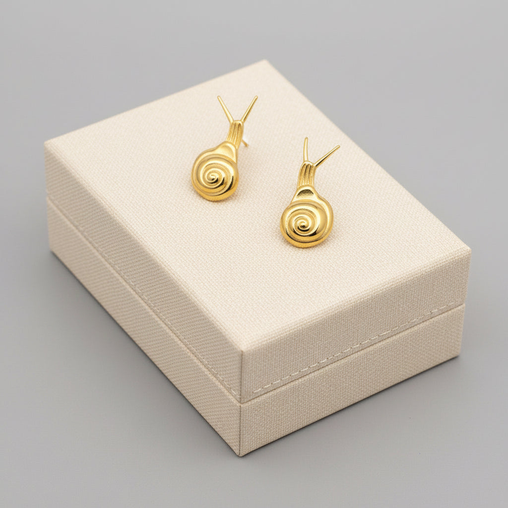 Gold snail-shaped earrings held in a hand against a textured gray background