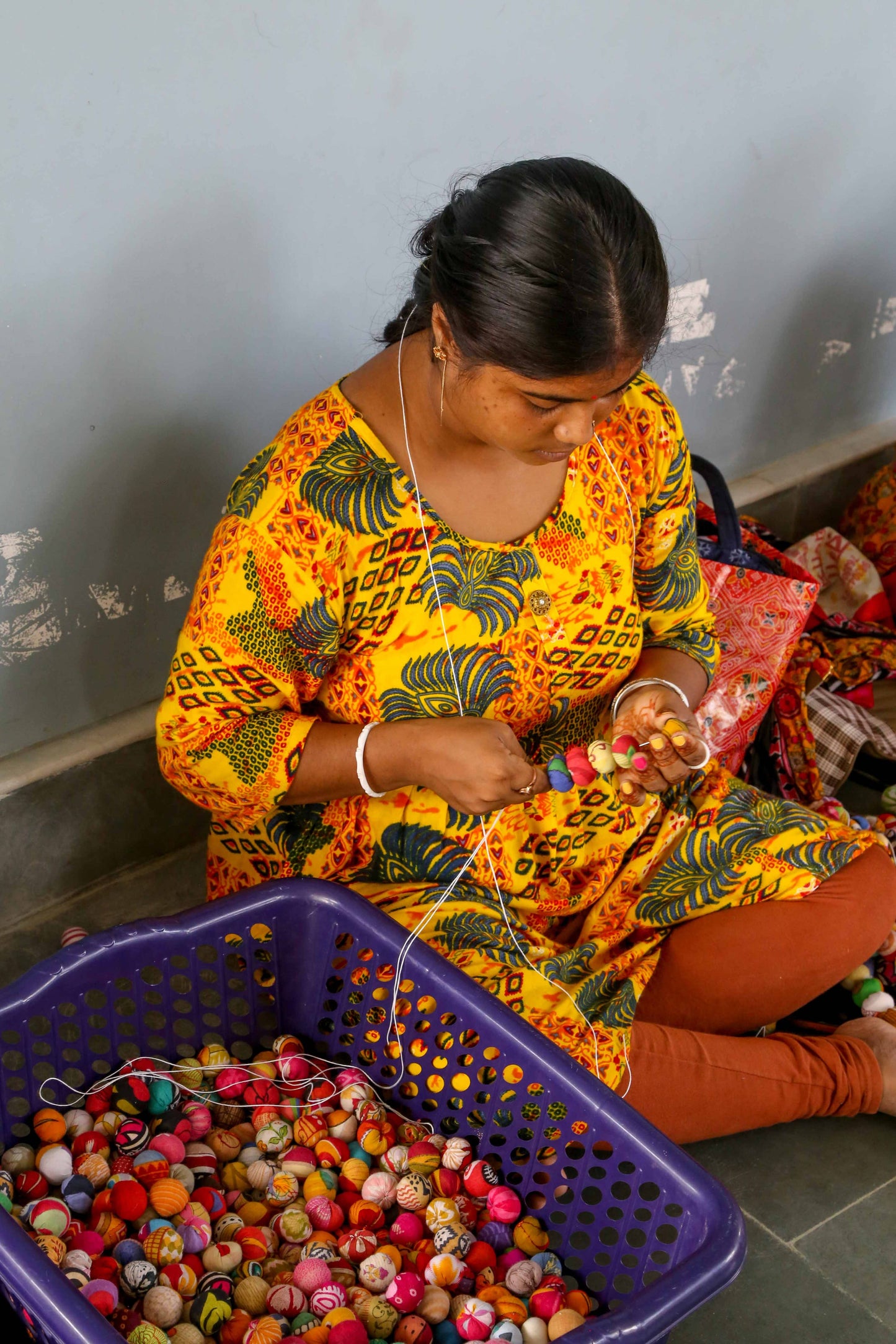 An Indian woman in a colorful patterned shirt sorting beads in a purple basket.