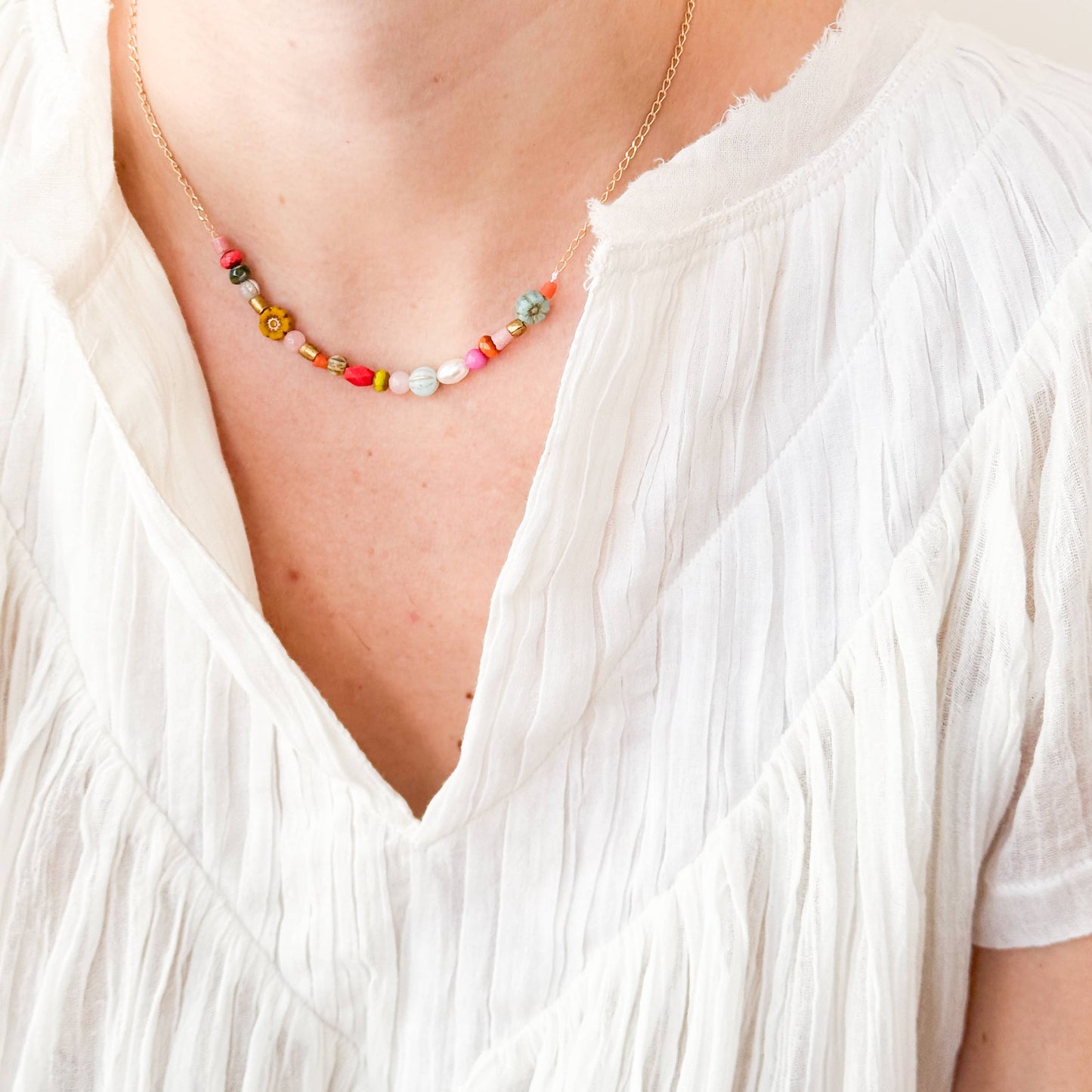 Blue and mustard flower necklace styled against white linen shirt