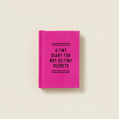Mini pink diary with black text, "A Tiny Diary For Not-So-Tiny Secrets" on a light beige background