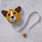 Crochet dog measuring tape with floppy 3D ears and smiling face, shown on a craft table