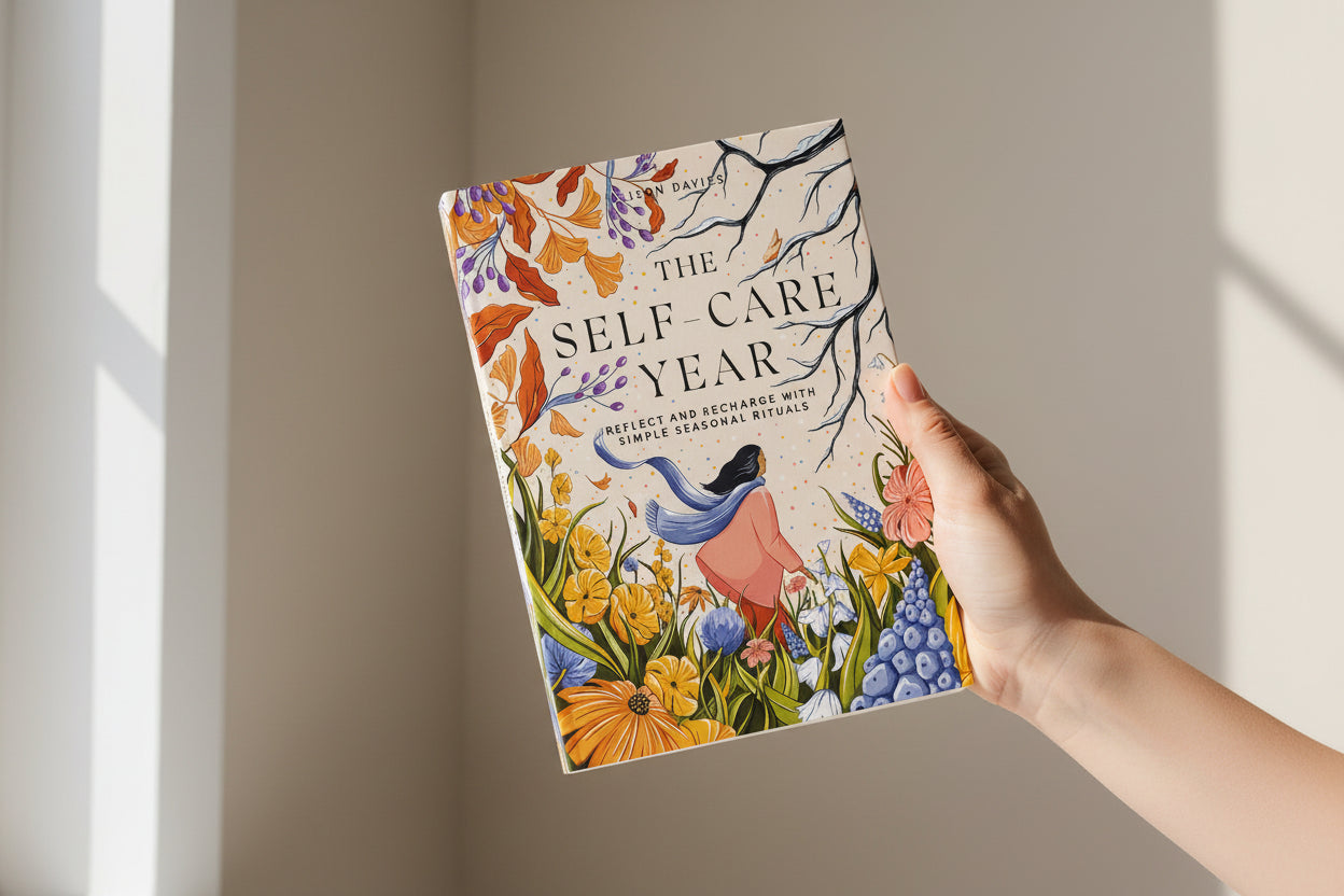 Hand holding a book titled 'The Self-Care Year' with a colorful cover against a neutral background