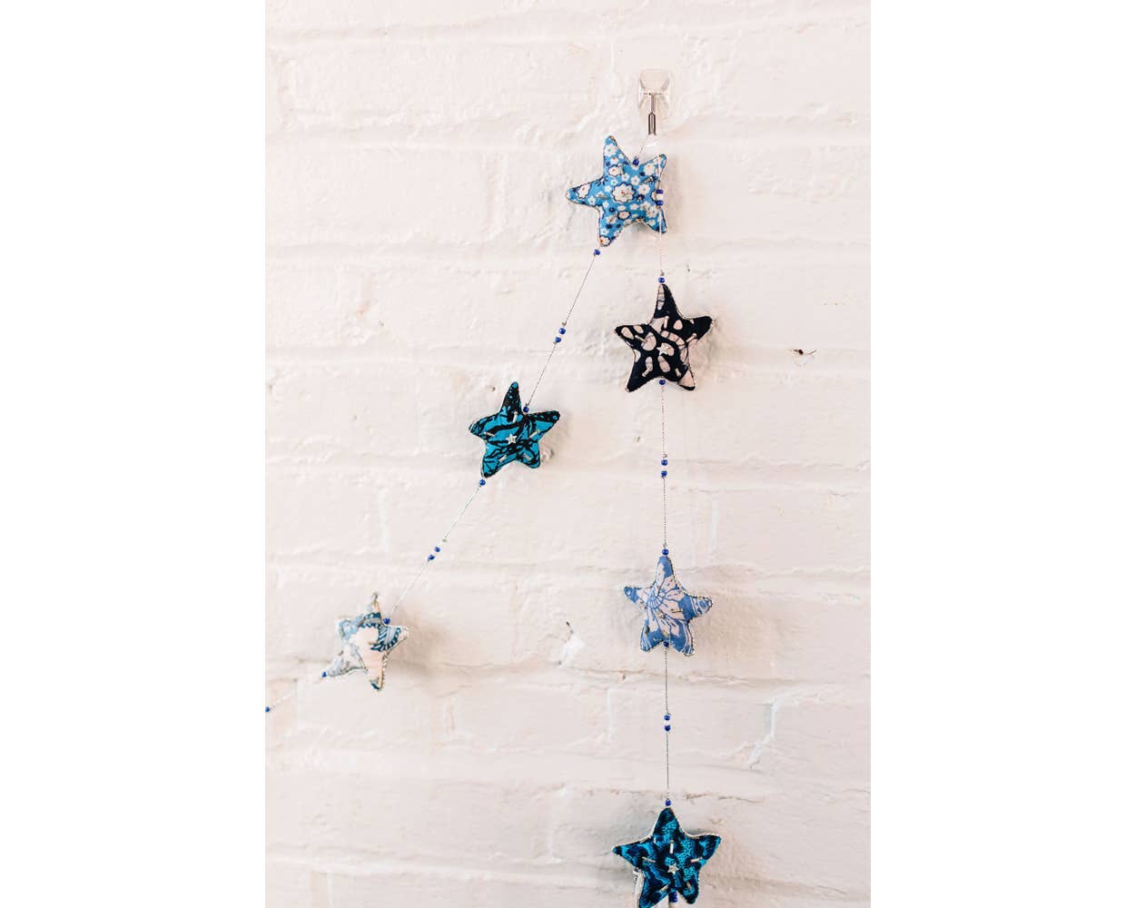 The Embroidered Star Garland hanging from a white brick wall