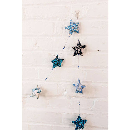The Embroidered Star Garland hanging from a white brick wall