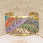 Gold-toned bracelet with colorful embroidered leaves on a beige fabric background