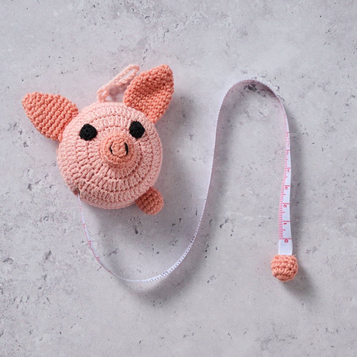 Crocheted pig measuring tape on a gray surface