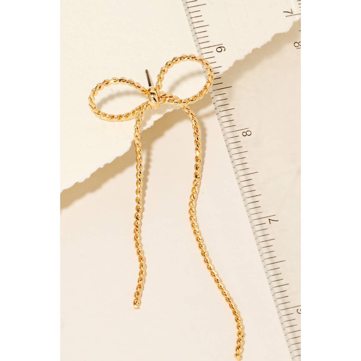 Close-up of delicate gold dangle ribbon bow earrings against neutral background