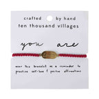 Red macrame bracelet with brass charm engraved “loved,” handcrafted in Nepal