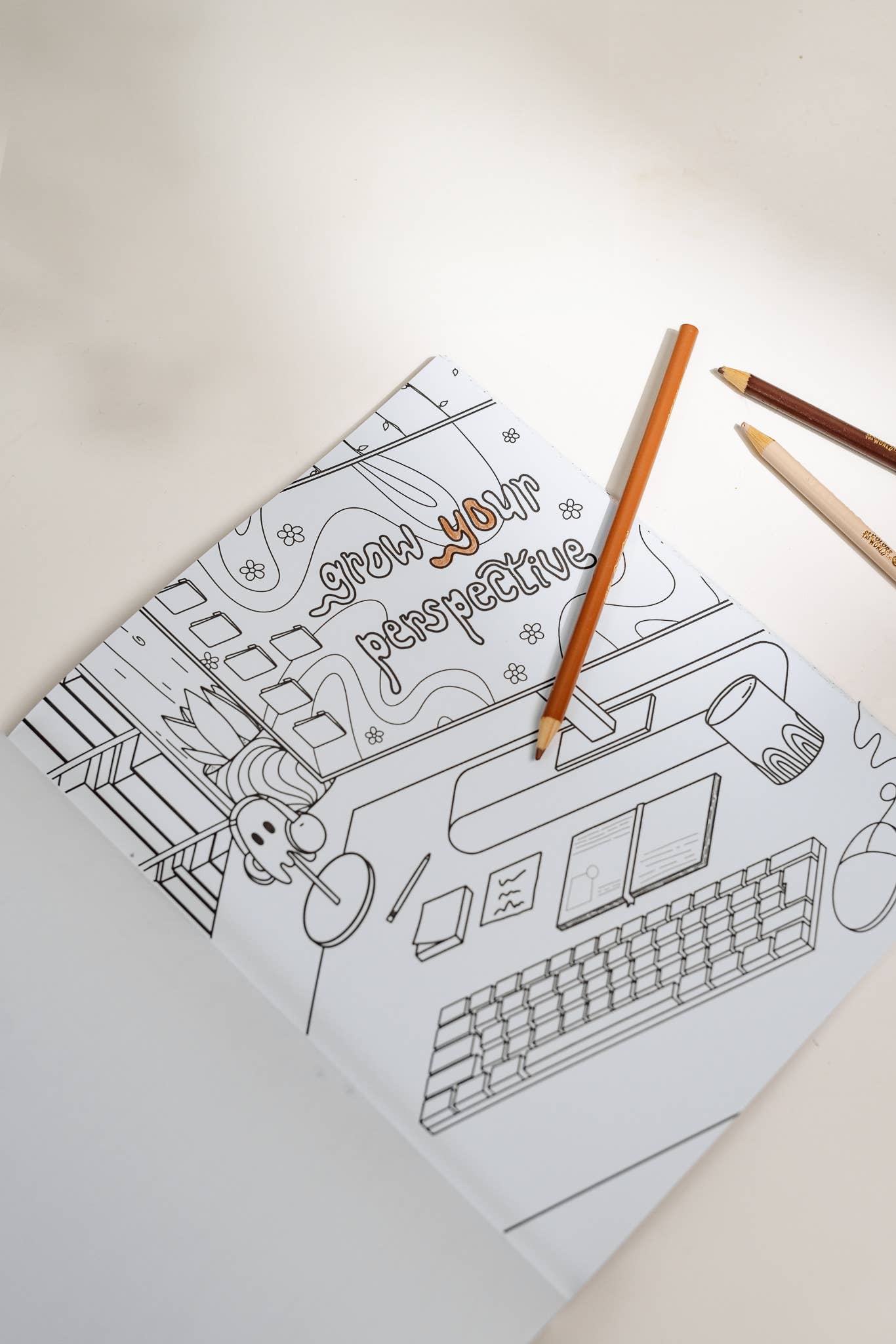 Coloring book with a design of a computer and text on a light surface with colored pencils.